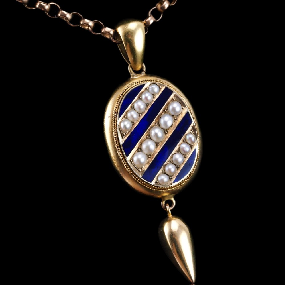 A Victorian 15ct gold oval pendant featuring diagonal stripes of royal blue enamel and seed pearls with a suspended gold drop.