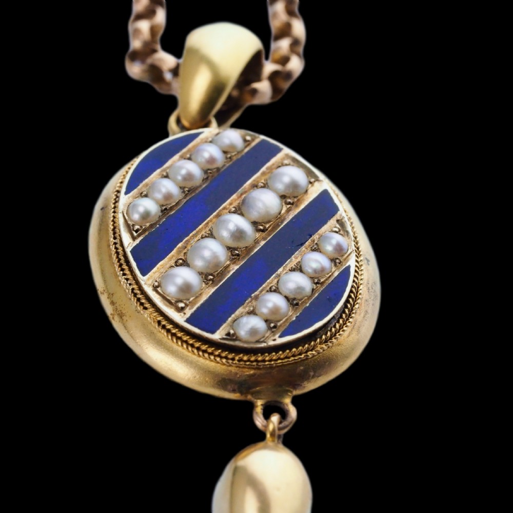 A Victorian 15ct gold oval pendant featuring diagonal stripes of royal blue enamel and seed pearls with a suspended gold drop. View V