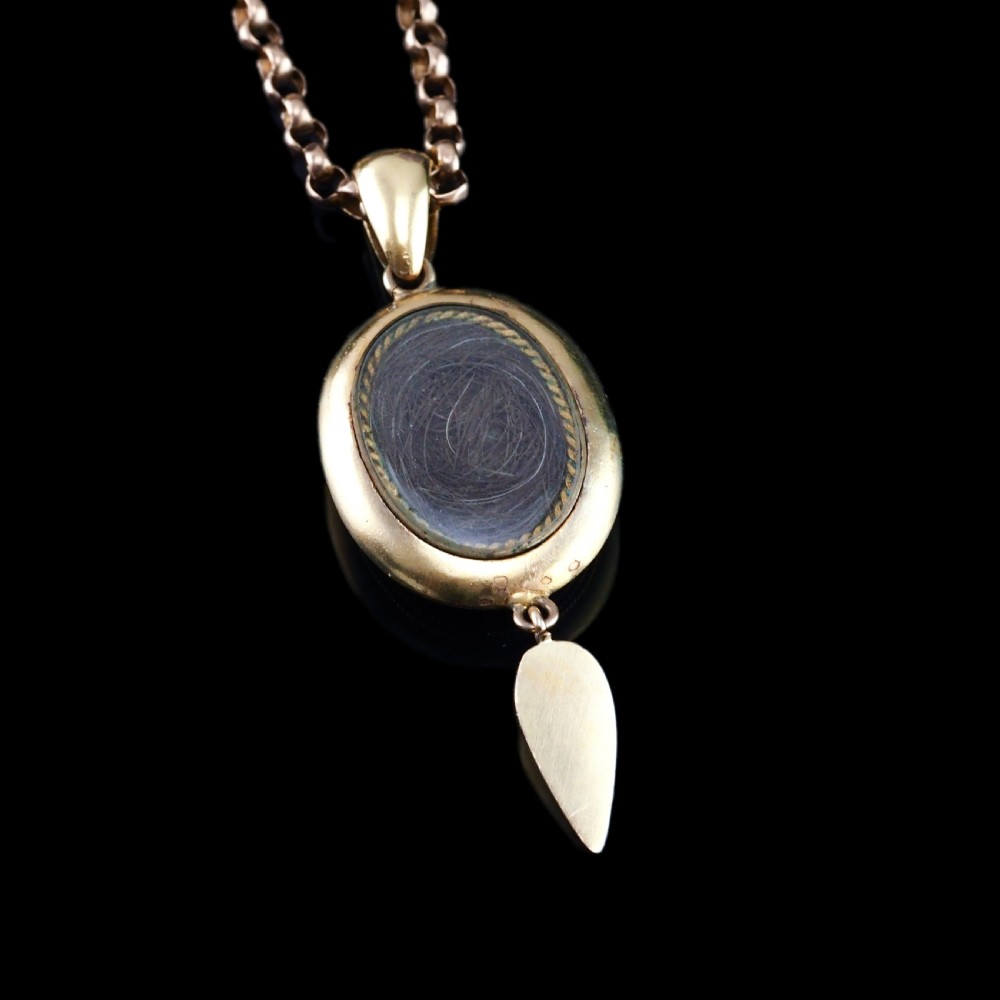 A Victorian 15ct gold oval pendant featuring diagonal stripes of royal blue enamel and seed pearls with a suspended gold drop. View VI