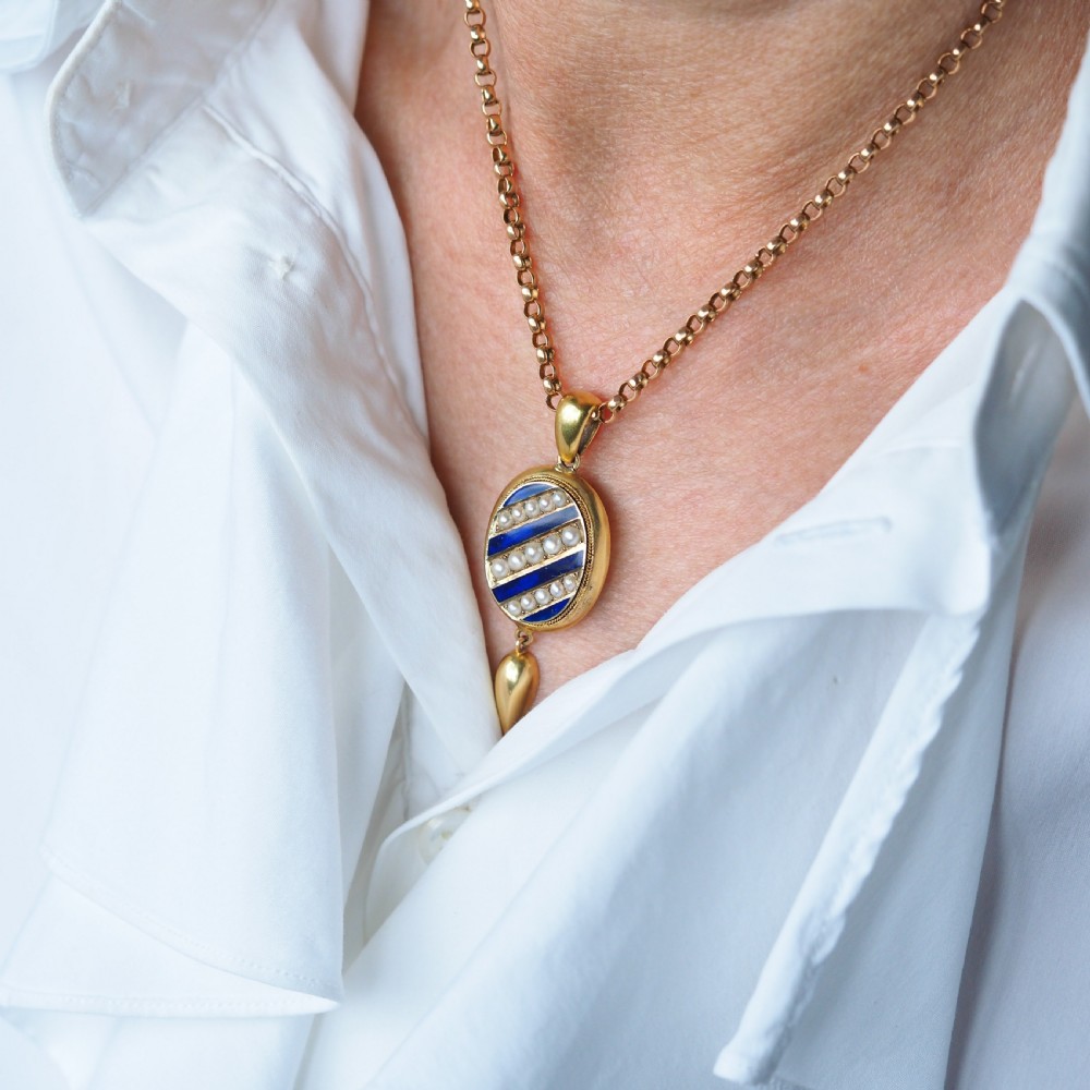 A Victorian 15ct gold oval pendant featuring diagonal stripes of royal blue enamel and seed pearls with a suspended gold drop. View IX