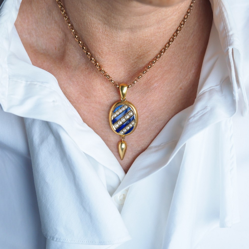 A Victorian 15ct gold oval pendant featuring diagonal stripes of royal blue enamel and seed pearls with a suspended gold drop. View X
