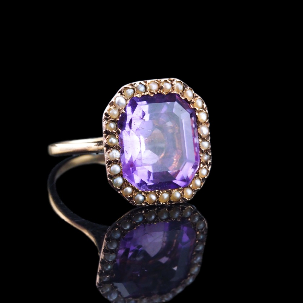 An Edwardian 18ct gold ring featuring a central emerald-cut purple amethyst surrounded by a halo of small seed pearls. View VIII