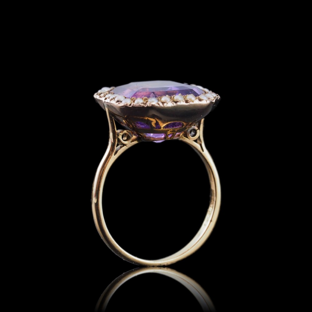 An Edwardian 18ct gold ring featuring a central emerald-cut purple amethyst surrounded by a halo of small seed pearls. View IX