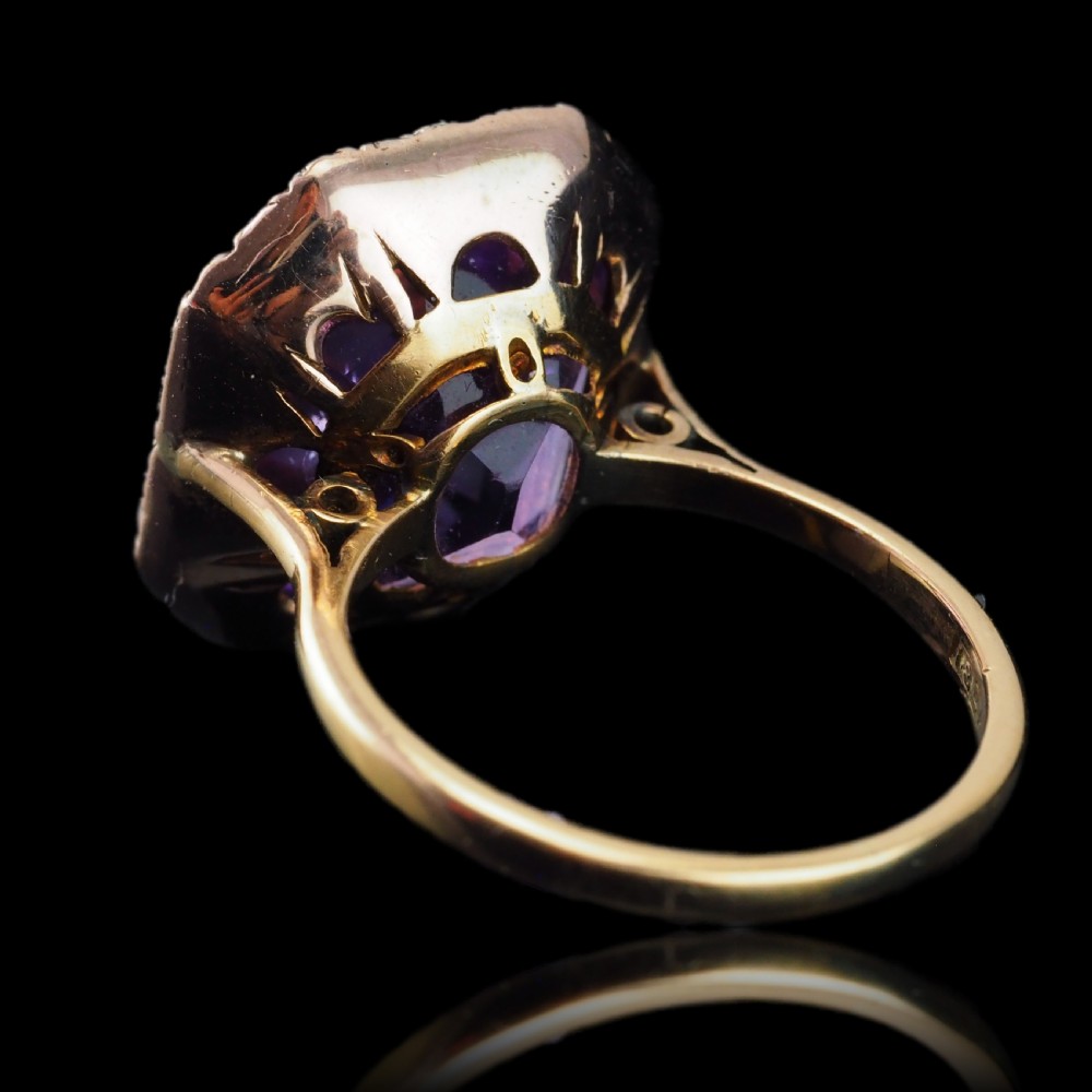 An Edwardian 18ct gold ring featuring a central emerald-cut purple amethyst surrounded by a halo of small seed pearls. View XIV