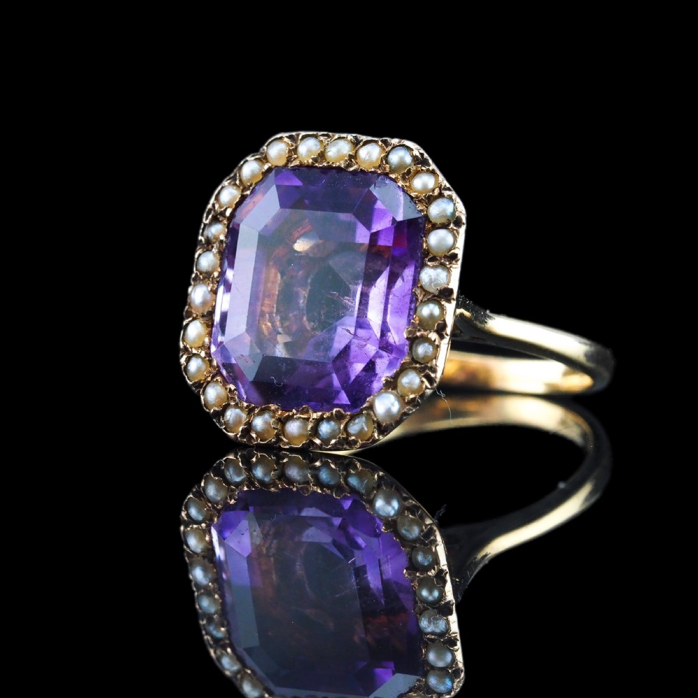 An Edwardian 18ct gold ring featuring a central emerald-cut purple amethyst surrounded by a halo of small seed pearls. View XVI