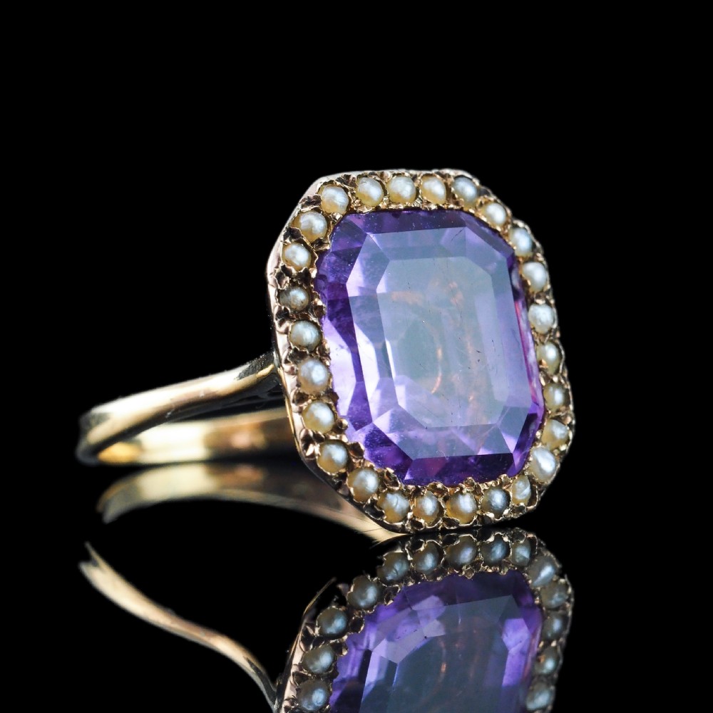 An Edwardian 18ct gold ring featuring a central emerald-cut purple amethyst surrounded by a halo of small seed pearls. View XVII