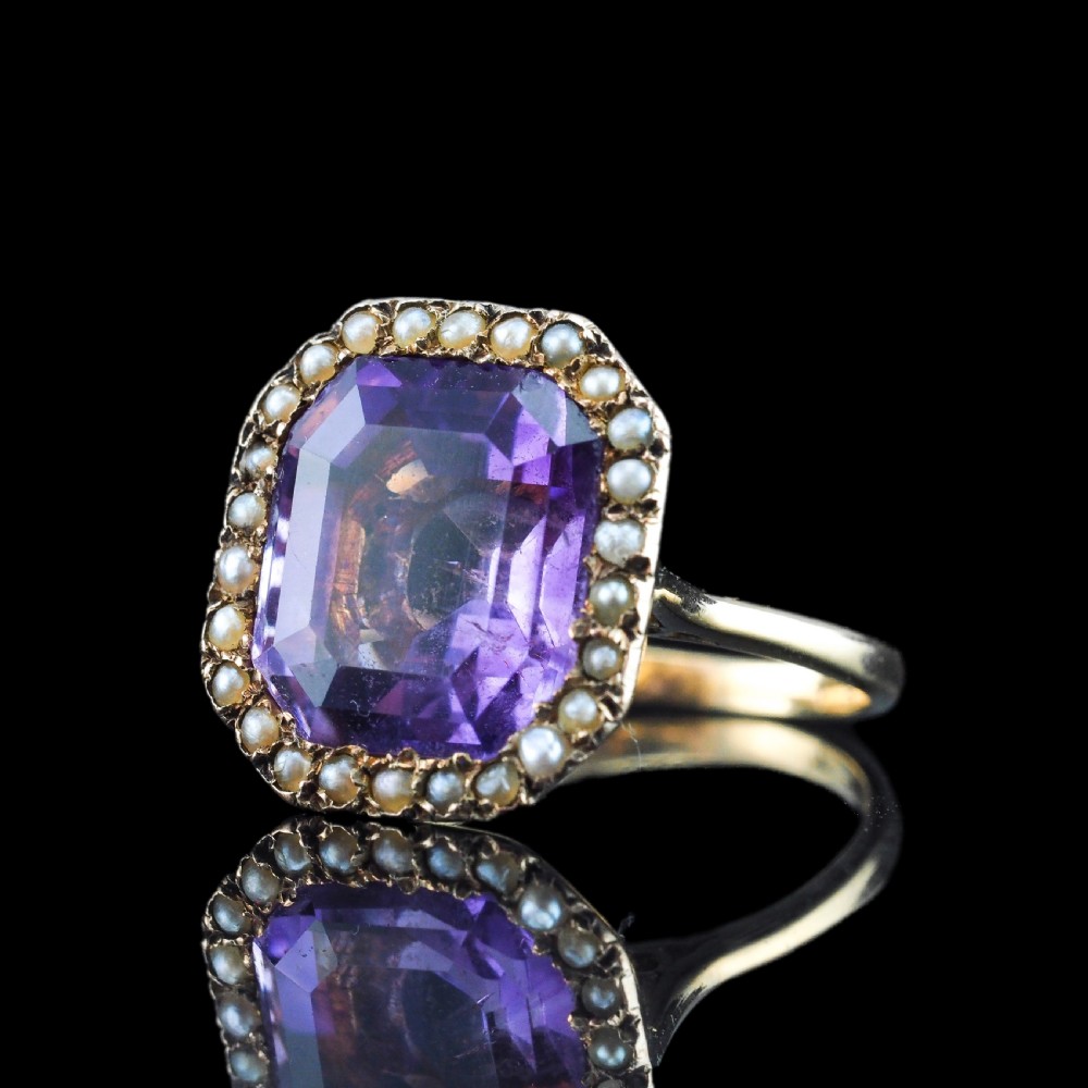 An Edwardian 18ct gold ring featuring a central emerald-cut purple amethyst surrounded by a halo of small seed pearls. View XVIII