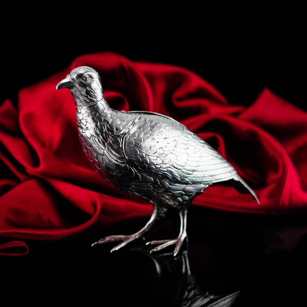 A solid silver model of a partridge with chased feather detailing standing on two feet with a hinged compartment lid along its back. View III
