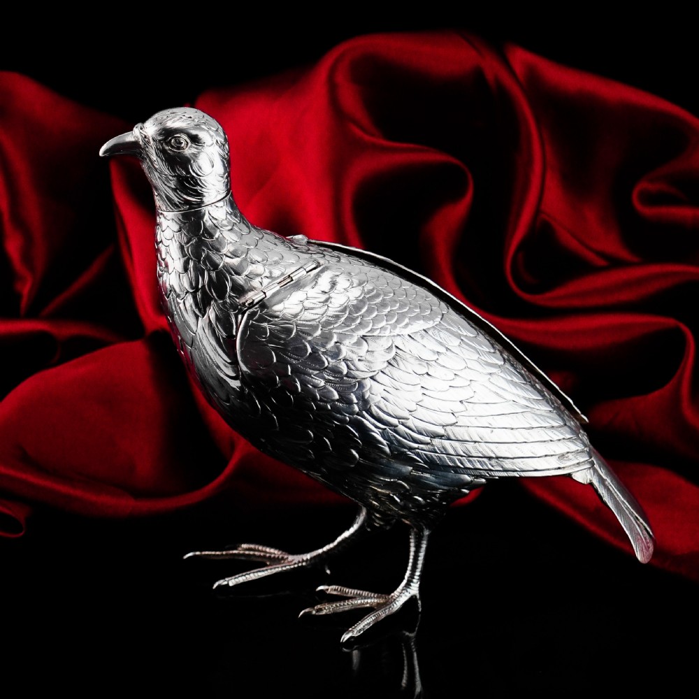 A solid silver model of a partridge with chased feather detailing standing on two feet with a hinged compartment lid along its back. View V