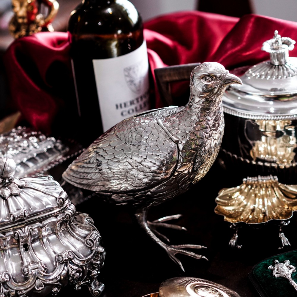 A solid silver model of a partridge with chased feather detailing standing on two feet with a hinged compartment lid along its back. View VI