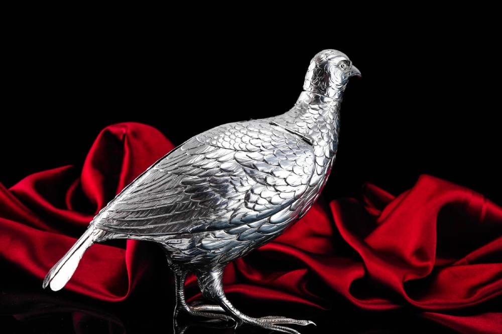 A solid silver model of a partridge with chased feather detailing standing on two feet with a hinged compartment lid along its back. View XXIII