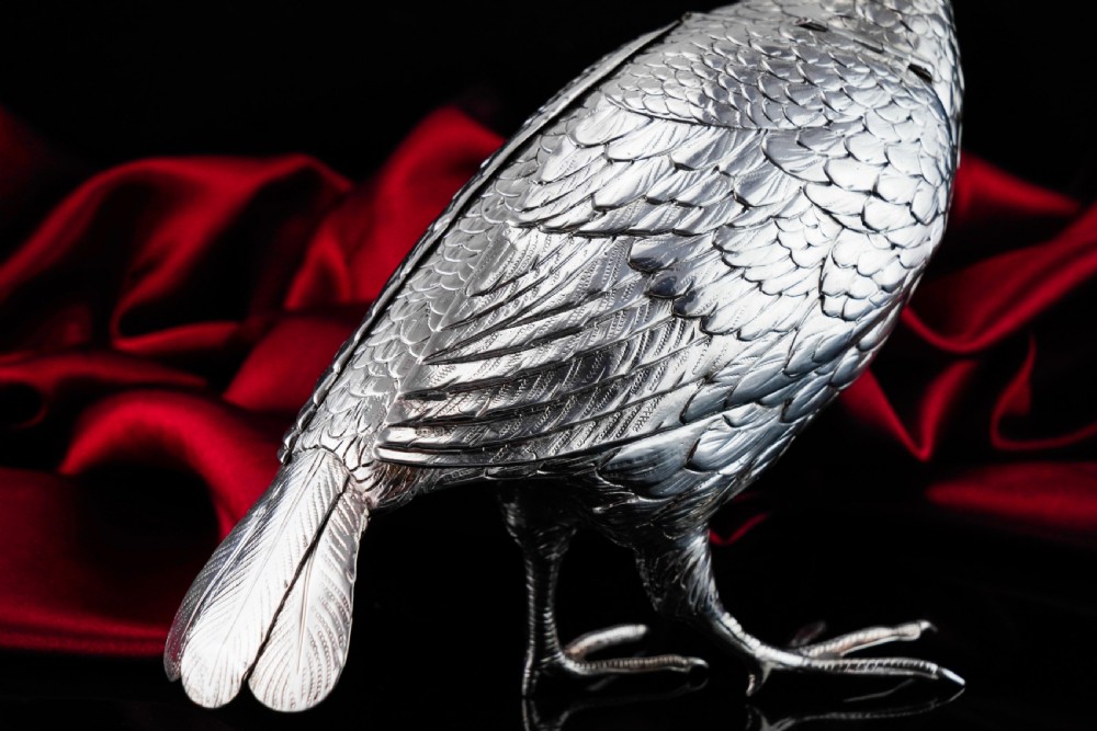 A solid silver model of a partridge with chased feather detailing standing on two feet with a hinged compartment lid along its back. View XXVII