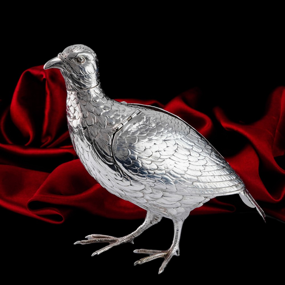 A solid silver model of a partridge with chased feather detailing standing on two feet with a hinged compartment lid along its back. View XXIX