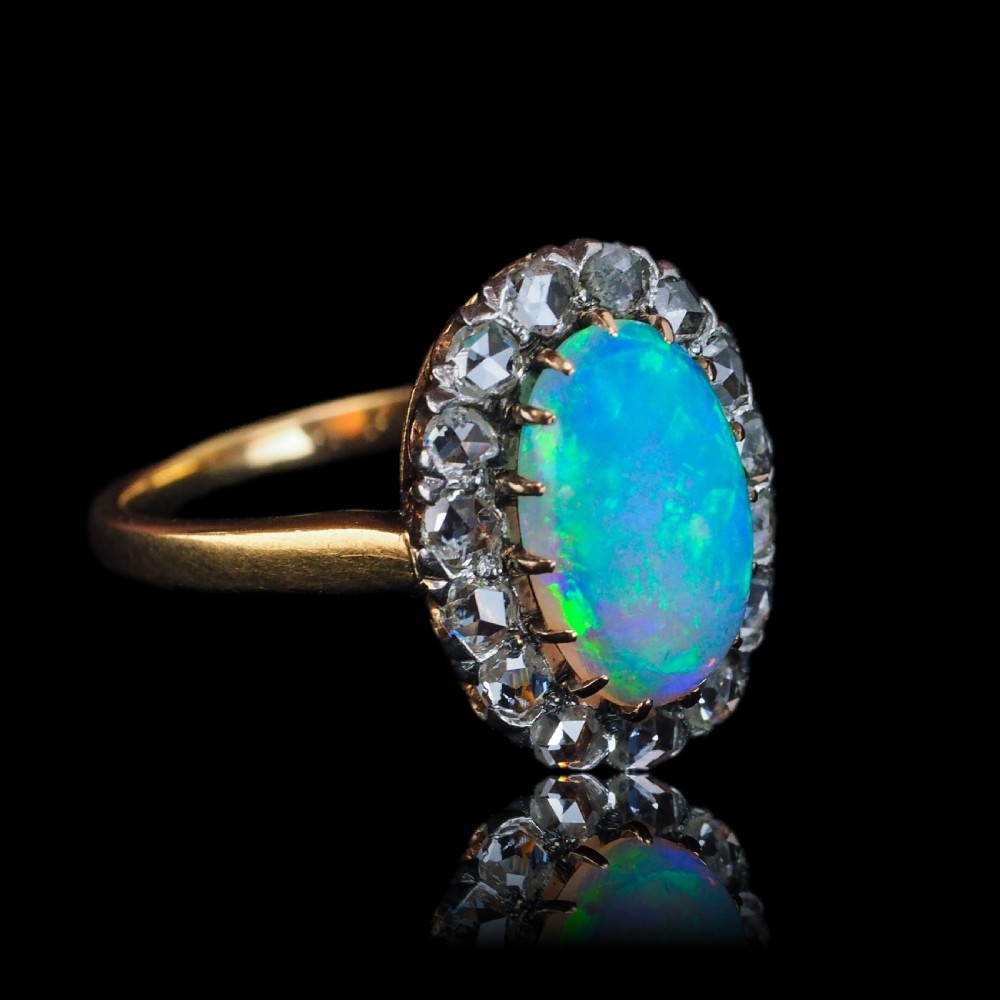 Victorian 18k gold cluster ring featuring an oval cabochon opal surrounded by a halo of rose-cut diamonds. View X