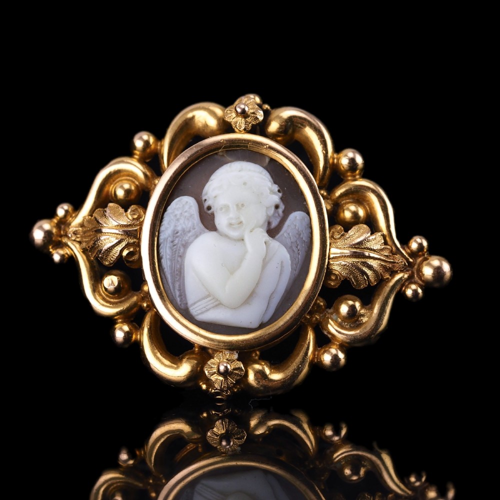 An oval Victorian shell cameo depicting a relief-carved cherub, mounted in an 18ct gold frame with scrollwork and leaf motifs.