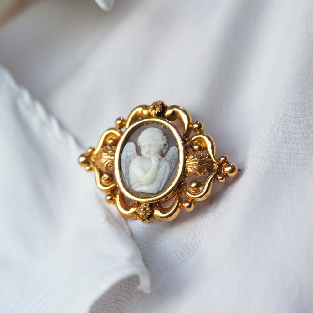 An oval Victorian shell cameo depicting a relief-carved cherub, mounted in an 18ct gold frame with scrollwork and leaf motifs. View V