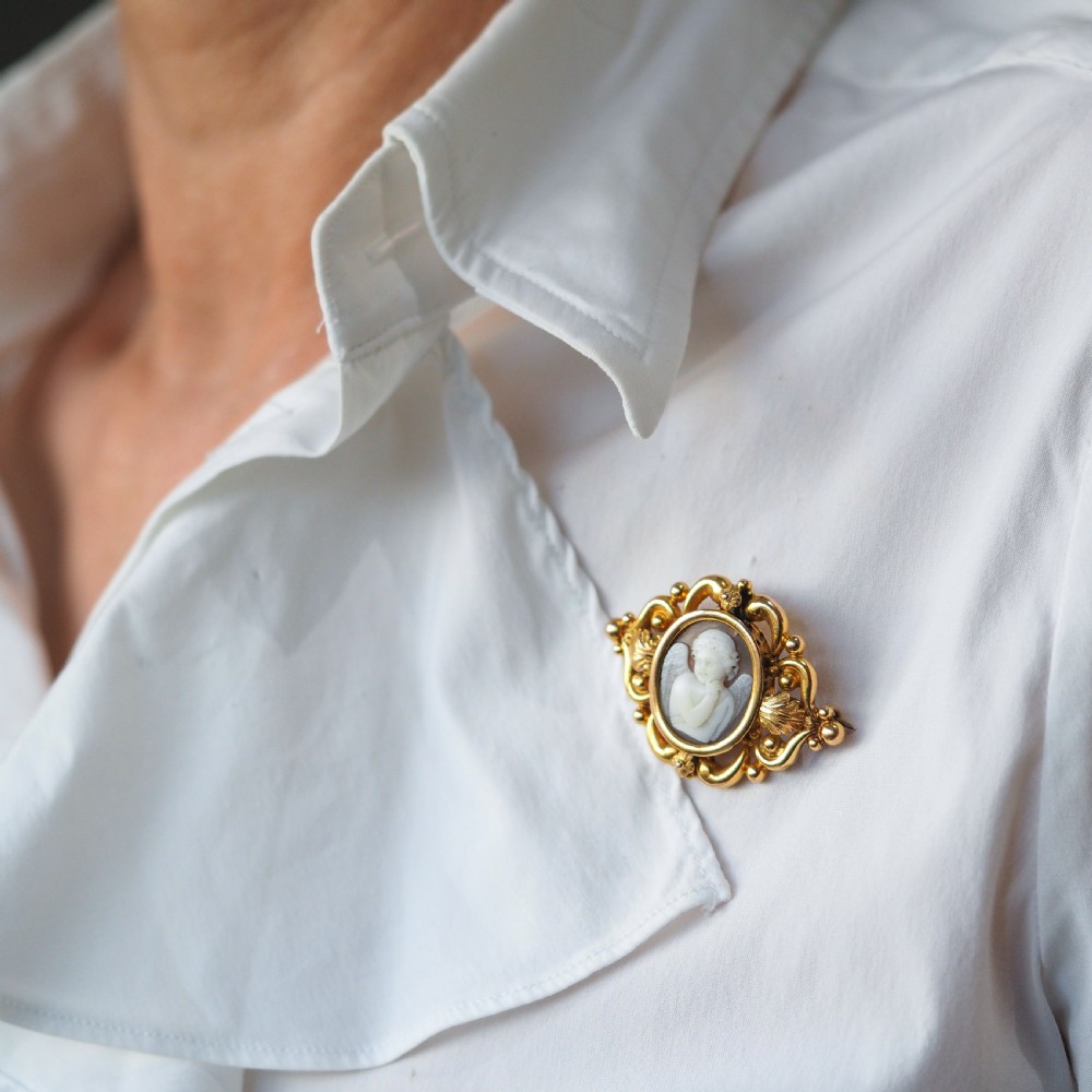 An oval Victorian shell cameo depicting a relief-carved cherub, mounted in an 18ct gold frame with scrollwork and leaf motifs. View VI