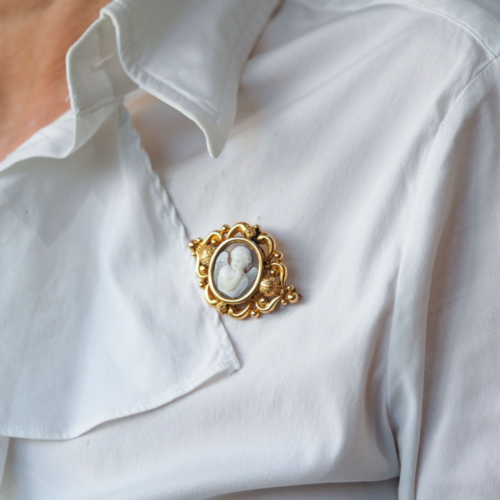 An oval Victorian shell cameo depicting a relief-carved cherub, mounted in an 18ct gold frame with scrollwork and leaf motifs. View VII