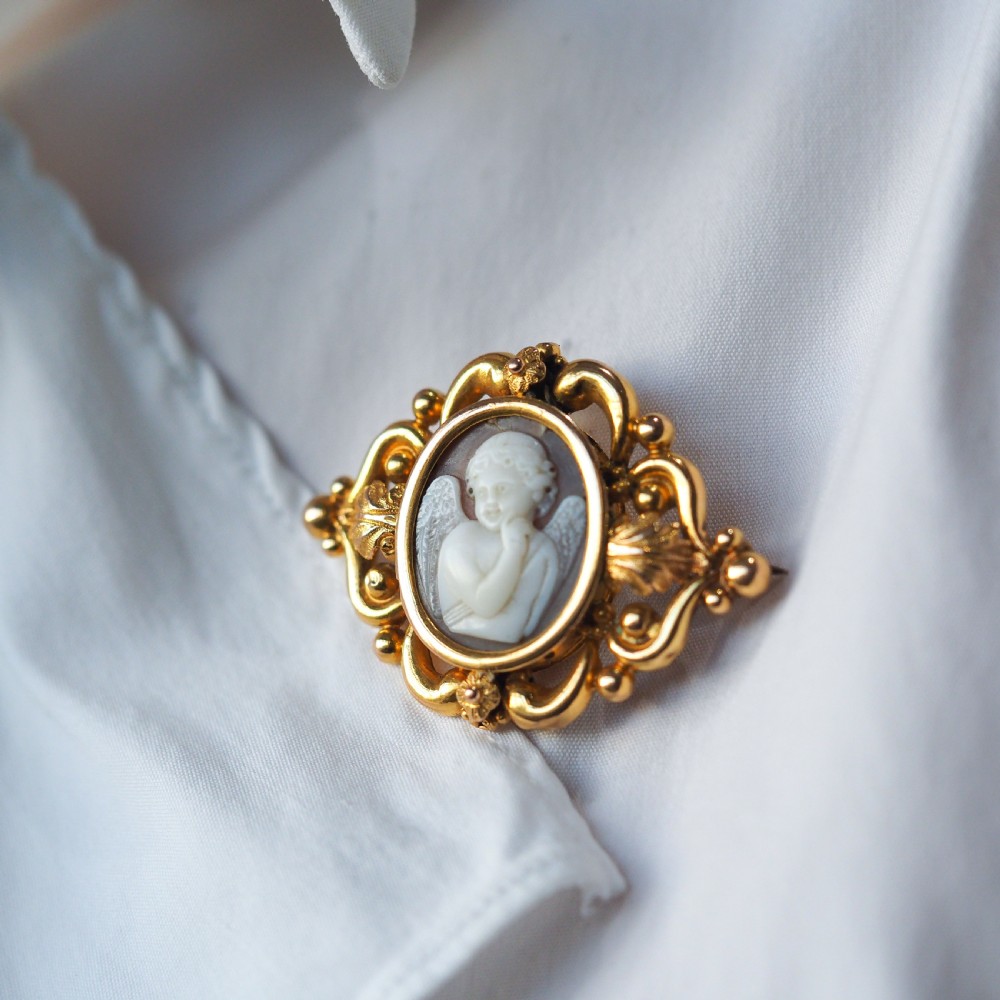 An oval Victorian shell cameo depicting a relief-carved cherub, mounted in an 18ct gold frame with scrollwork and leaf motifs. View VIII