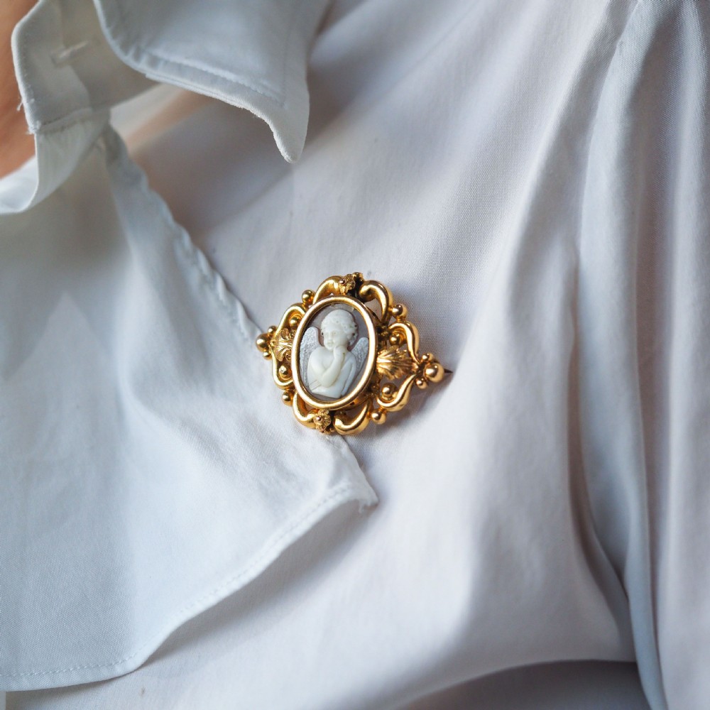 An oval Victorian shell cameo depicting a relief-carved cherub, mounted in an 18ct gold frame with scrollwork and leaf motifs. View IX