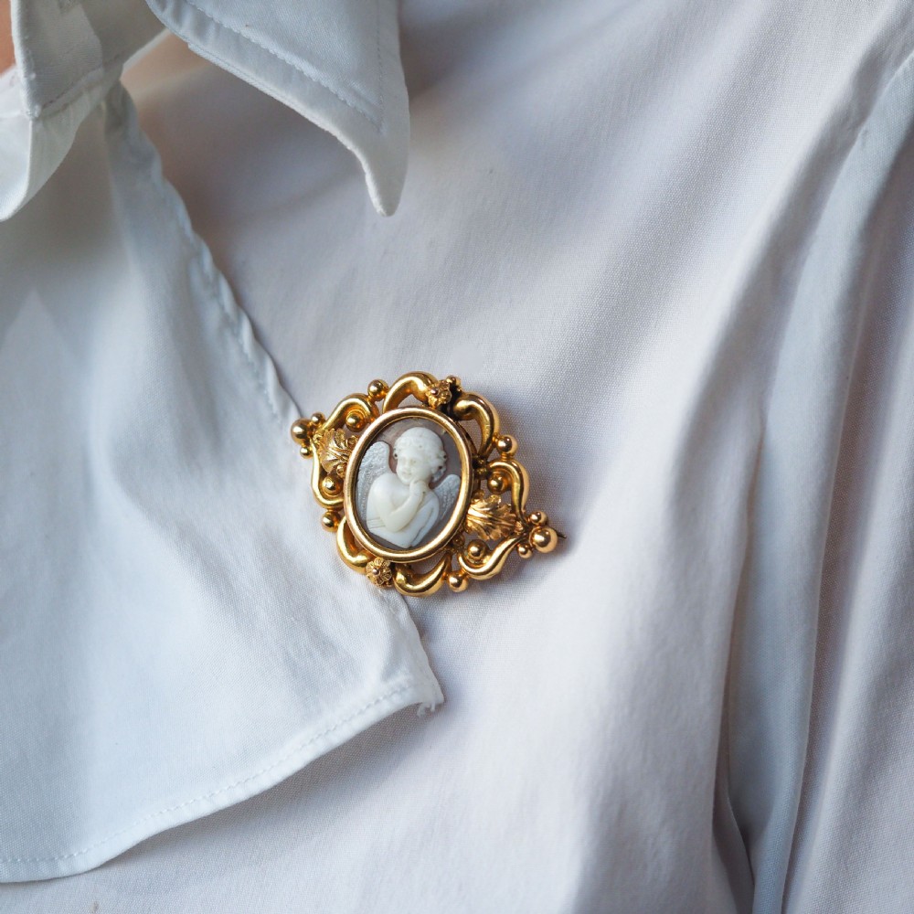 An oval Victorian shell cameo depicting a relief-carved cherub, mounted in an 18ct gold frame with scrollwork and leaf motifs. View X