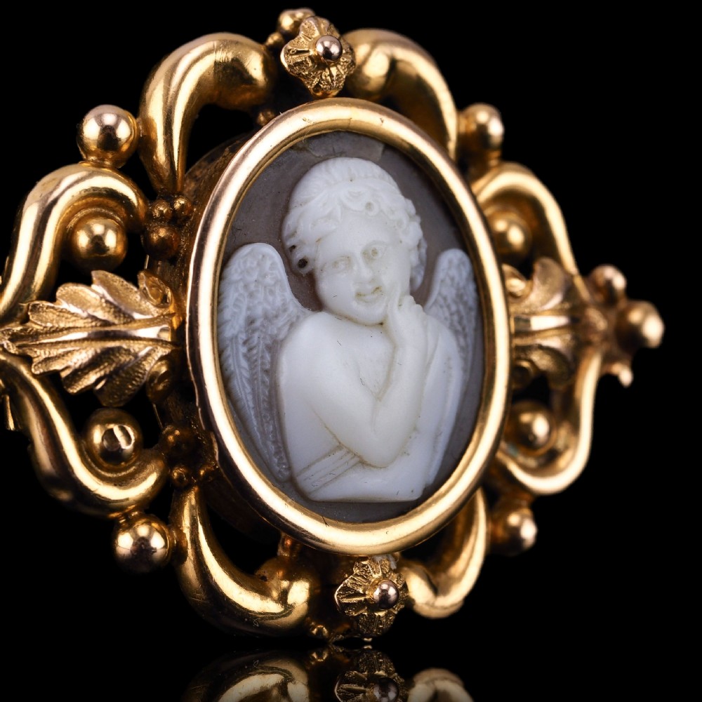 An oval Victorian shell cameo depicting a relief-carved cherub, mounted in an 18ct gold frame with scrollwork and leaf motifs. View XIV