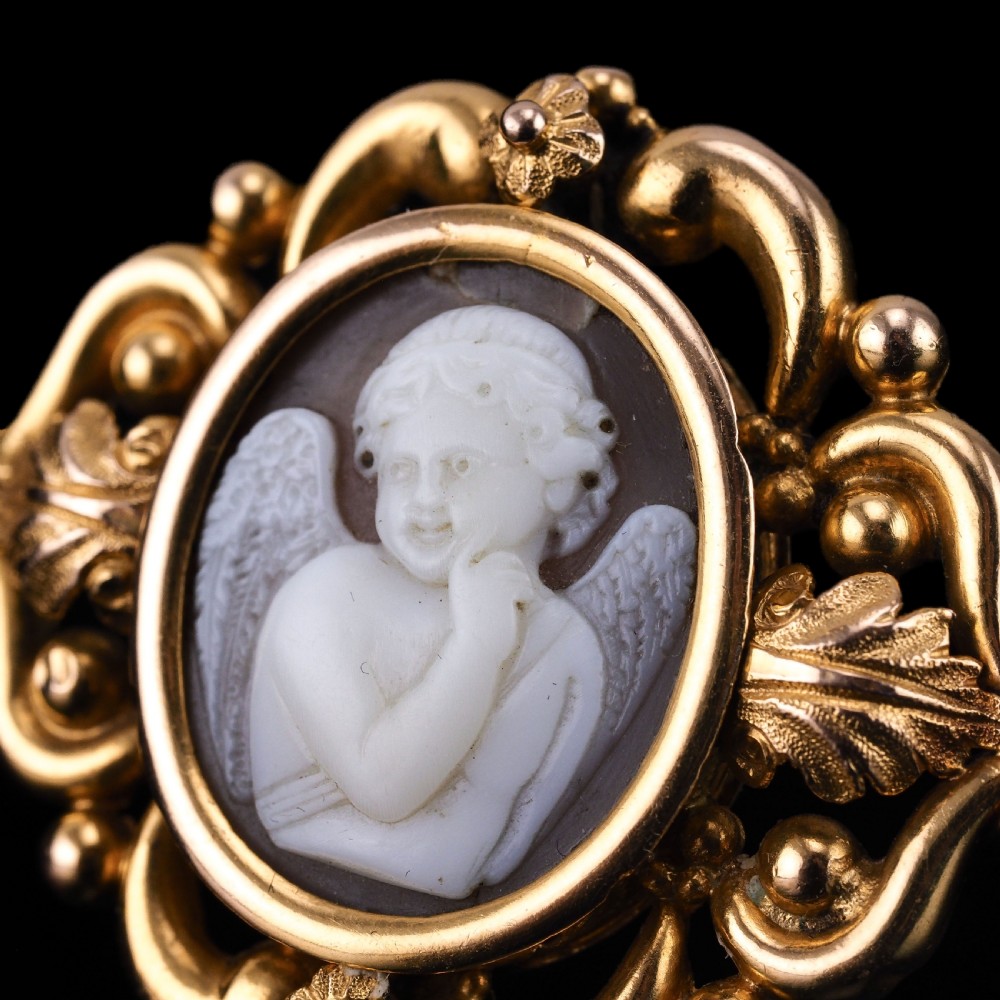 An oval Victorian shell cameo depicting a relief-carved cherub, mounted in an 18ct gold frame with scrollwork and leaf motifs. View XV