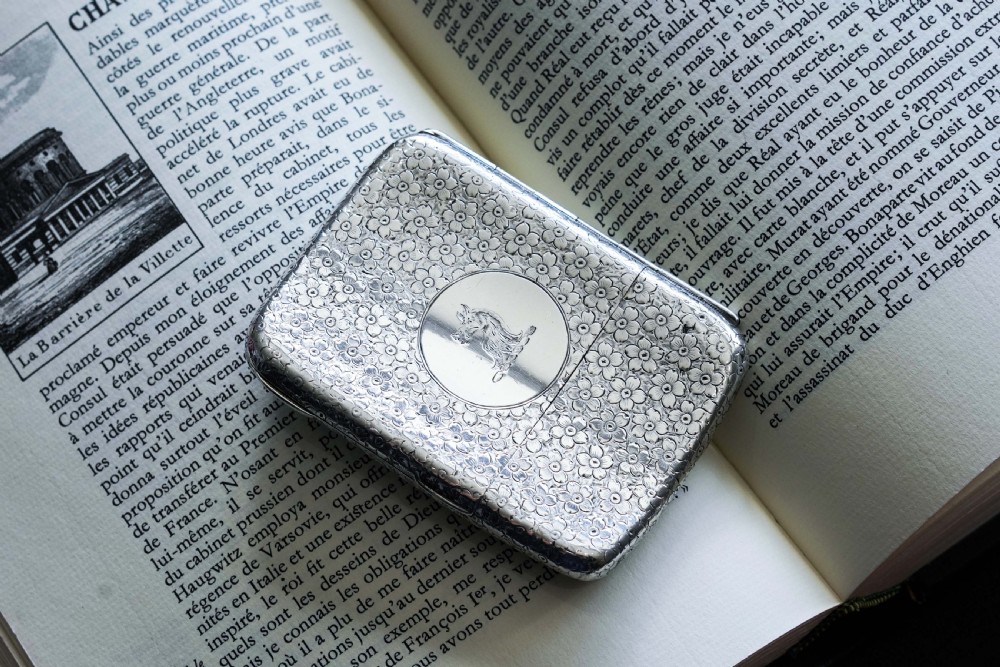 An antique Victorian sterling silver cigarette case decorated with an overall engraved floral pattern and a central oval cartouche containing a heraldic crest. View VII