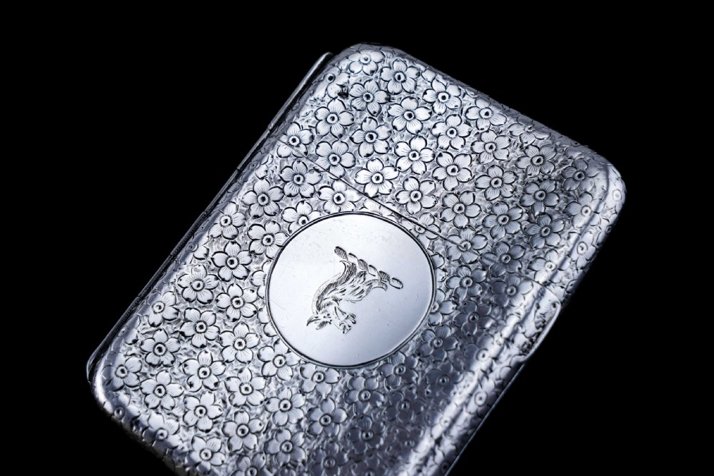 An antique Victorian sterling silver cigarette case decorated with an overall engraved floral pattern and a central oval cartouche containing a heraldic crest. View VIII