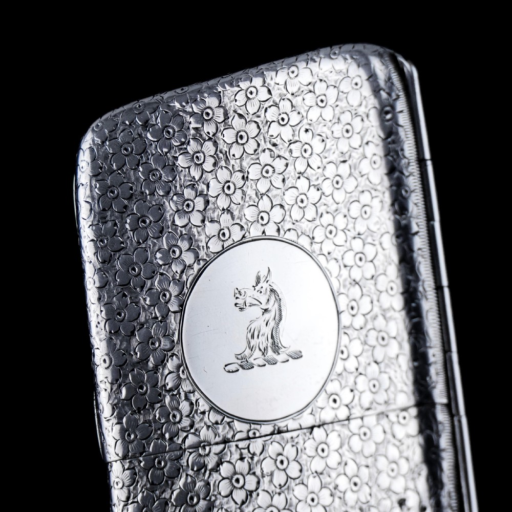 An antique Victorian sterling silver cigarette case decorated with an overall engraved floral pattern and a central oval cartouche containing a heraldic crest. View IX