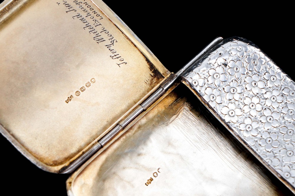 An antique Victorian sterling silver cigarette case decorated with an overall engraved floral pattern and a central oval cartouche containing a heraldic crest. View X