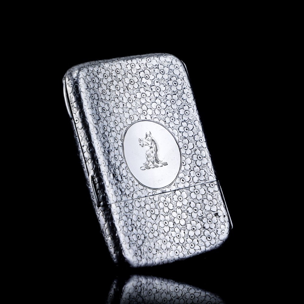 An antique Victorian sterling silver cigarette case decorated with an overall engraved floral pattern and a central oval cartouche containing a heraldic crest. View XIII