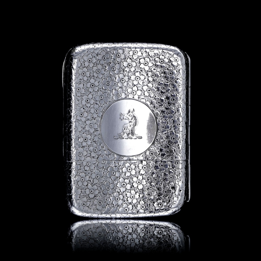 An antique Victorian sterling silver cigarette case decorated with an overall engraved floral pattern and a central oval cartouche containing a heraldic crest. View XVI