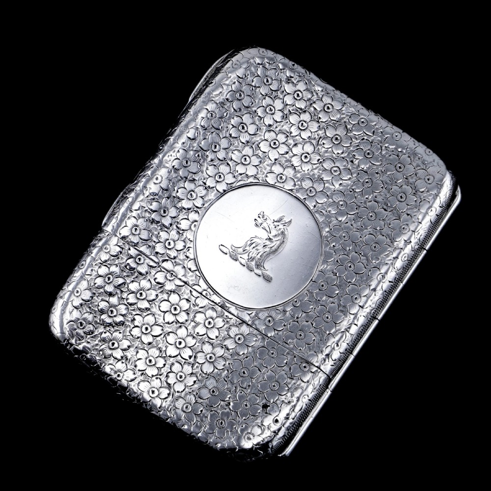 An antique Victorian sterling silver cigarette case decorated with an overall engraved floral pattern and a central oval cartouche containing a heraldic crest. View XVII