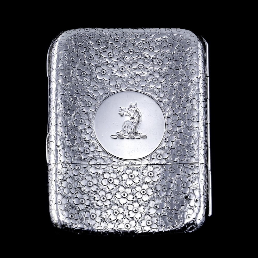 An antique Victorian sterling silver cigarette case decorated with an overall engraved floral pattern and a central oval cartouche containing a heraldic crest. View XVIII
