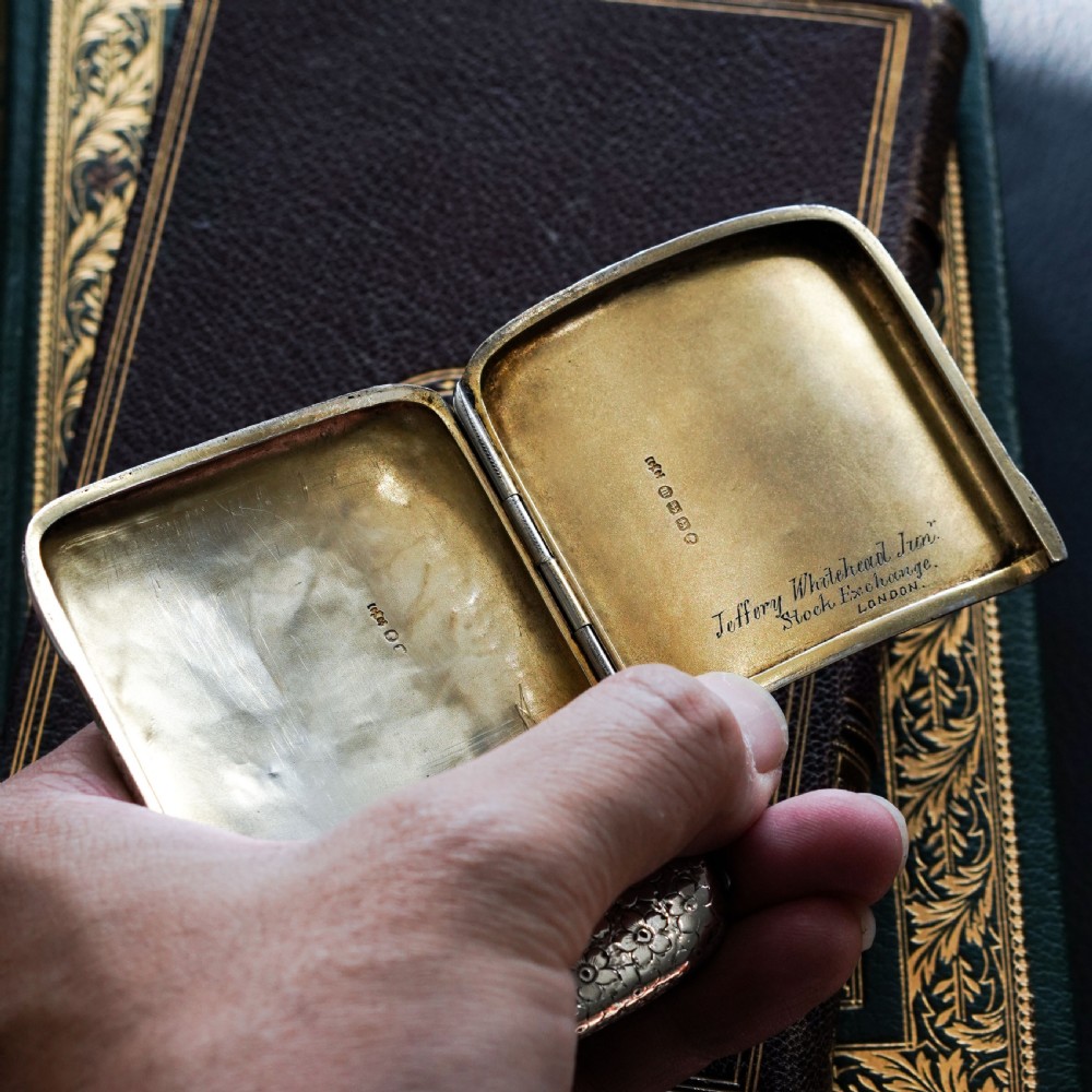 An antique Victorian sterling silver cigarette case decorated with an overall engraved floral pattern and a central oval cartouche containing a heraldic crest. View XIX