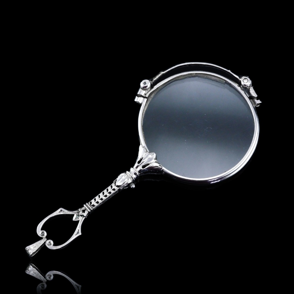 An Art Deco platinum lorgnette featuring a circular folding magnifying glass lens attached to a geometric handle set with small diamonds. View II