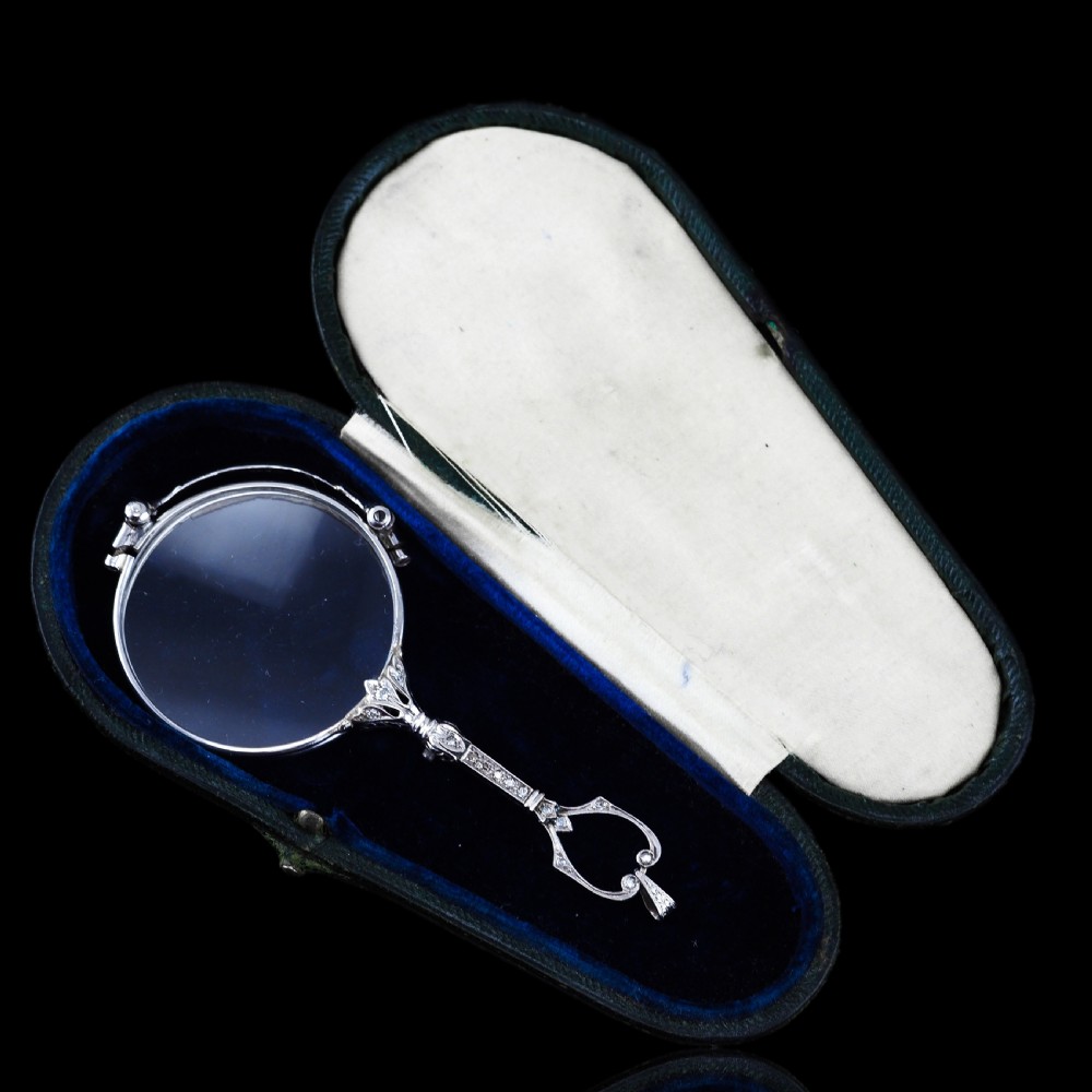An Art Deco platinum lorgnette featuring a circular folding magnifying glass lens attached to a geometric handle set with small diamonds. View IV