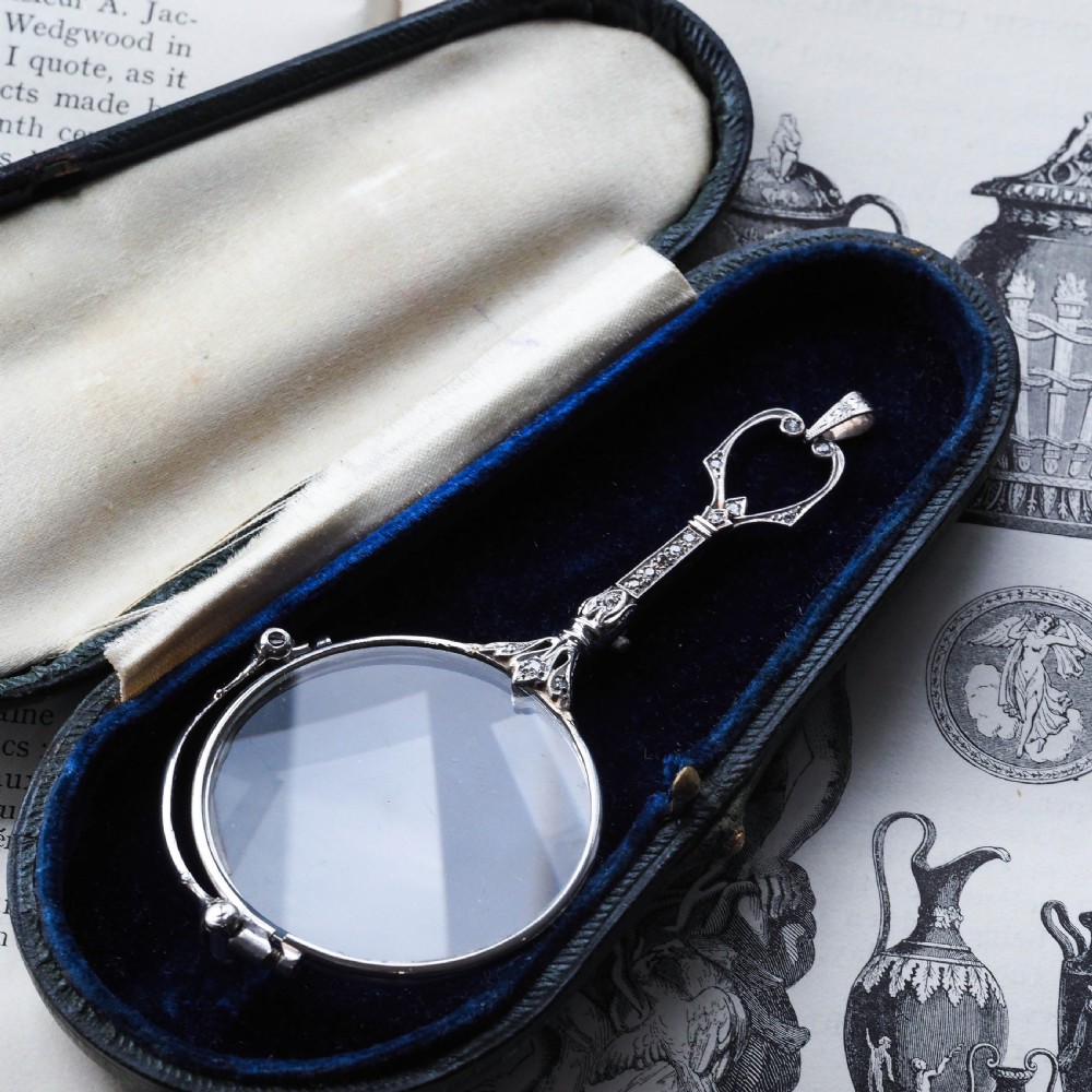 An Art Deco platinum lorgnette featuring a circular folding magnifying glass lens attached to a geometric handle set with small diamonds. View VII