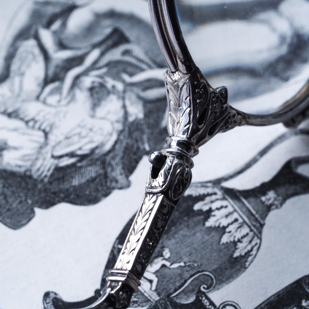 An Art Deco platinum lorgnette featuring a circular folding magnifying glass lens attached to a geometric handle set with small diamonds. View IX