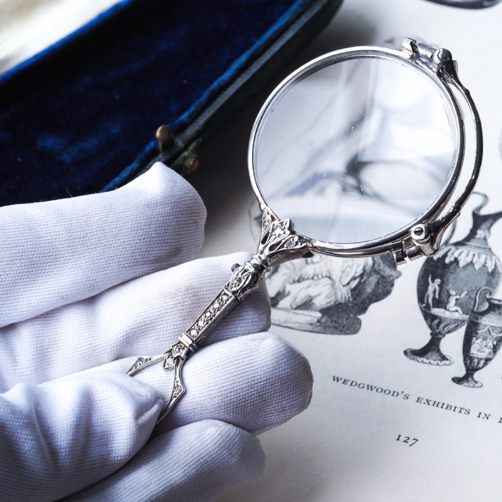An Art Deco platinum lorgnette featuring a circular folding magnifying glass lens attached to a geometric handle set with small diamonds. View XI