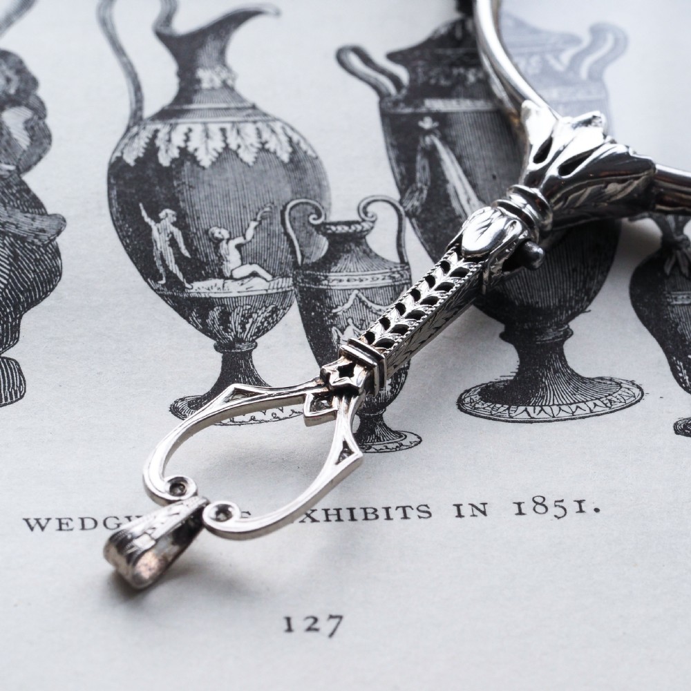 An Art Deco platinum lorgnette featuring a circular folding magnifying glass lens attached to a geometric handle set with small diamonds. View XII