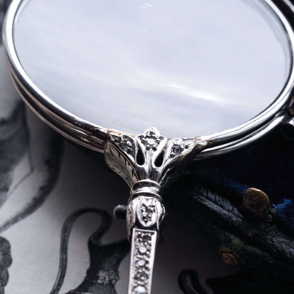 An Art Deco platinum lorgnette featuring a circular folding magnifying glass lens attached to a geometric handle set with small diamonds. View XIII
