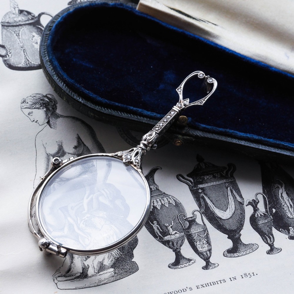 An Art Deco platinum lorgnette featuring a circular folding magnifying glass lens attached to a geometric handle set with small diamonds. View XIV