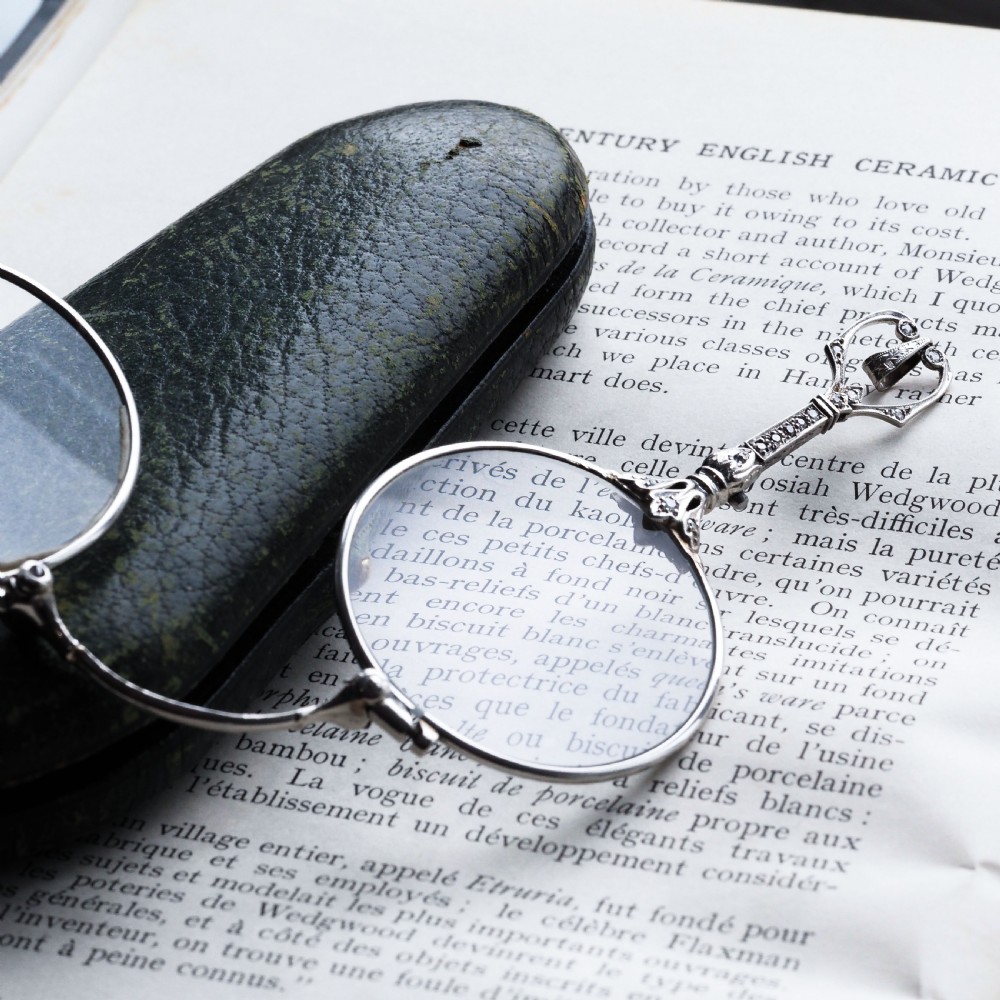 An Art Deco platinum lorgnette featuring a circular folding magnifying glass lens attached to a geometric handle set with small diamonds. View XV