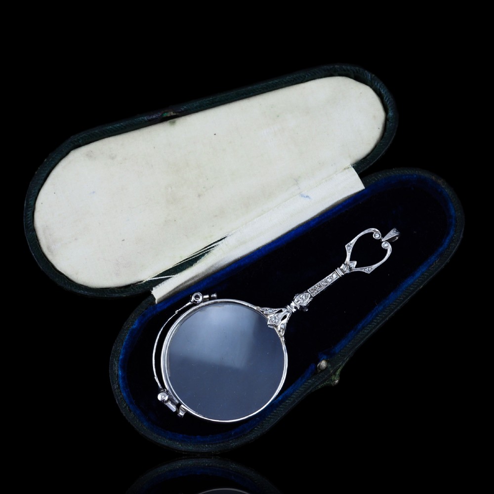 An Art Deco platinum lorgnette featuring a circular folding magnifying glass lens attached to a geometric handle set with small diamonds. View XIX