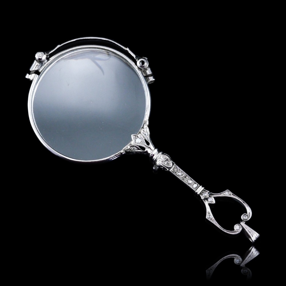 An Art Deco platinum lorgnette featuring a circular folding magnifying glass lens attached to a geometric handle set with small diamonds. View XX