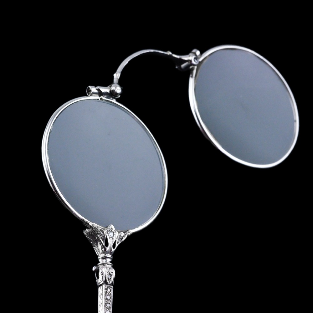 An Art Deco platinum lorgnette featuring a circular folding magnifying glass lens attached to a geometric handle set with small diamonds. View XXI
