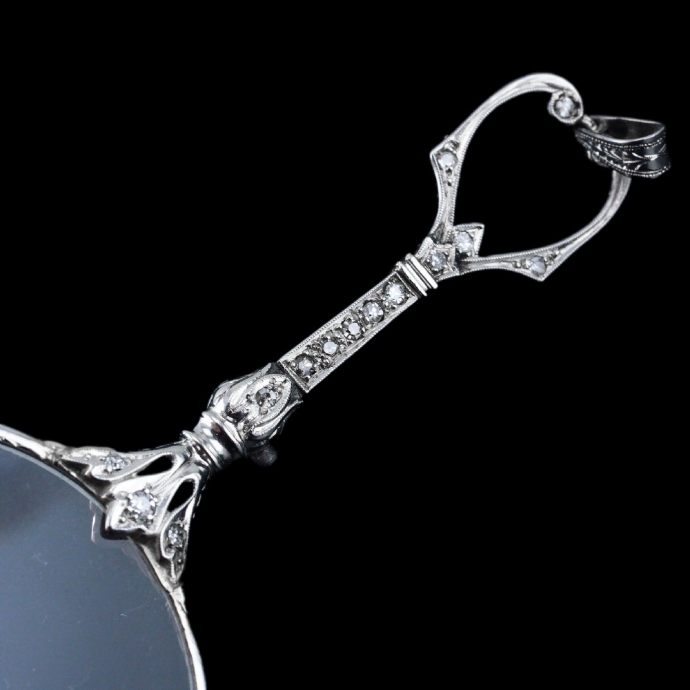 An Art Deco platinum lorgnette featuring a circular folding magnifying glass lens attached to a geometric handle set with small diamonds. View XXIII