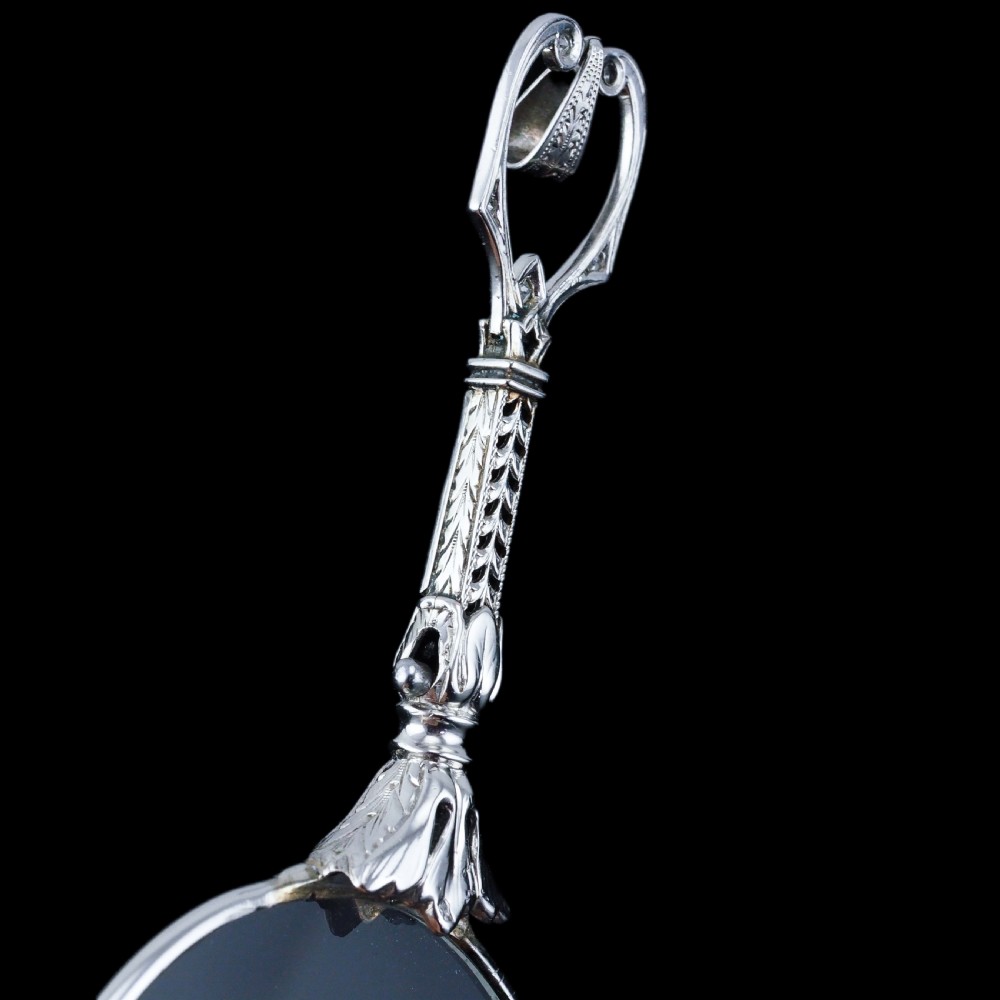 An Art Deco platinum lorgnette featuring a circular folding magnifying glass lens attached to a geometric handle set with small diamonds. View XXIV